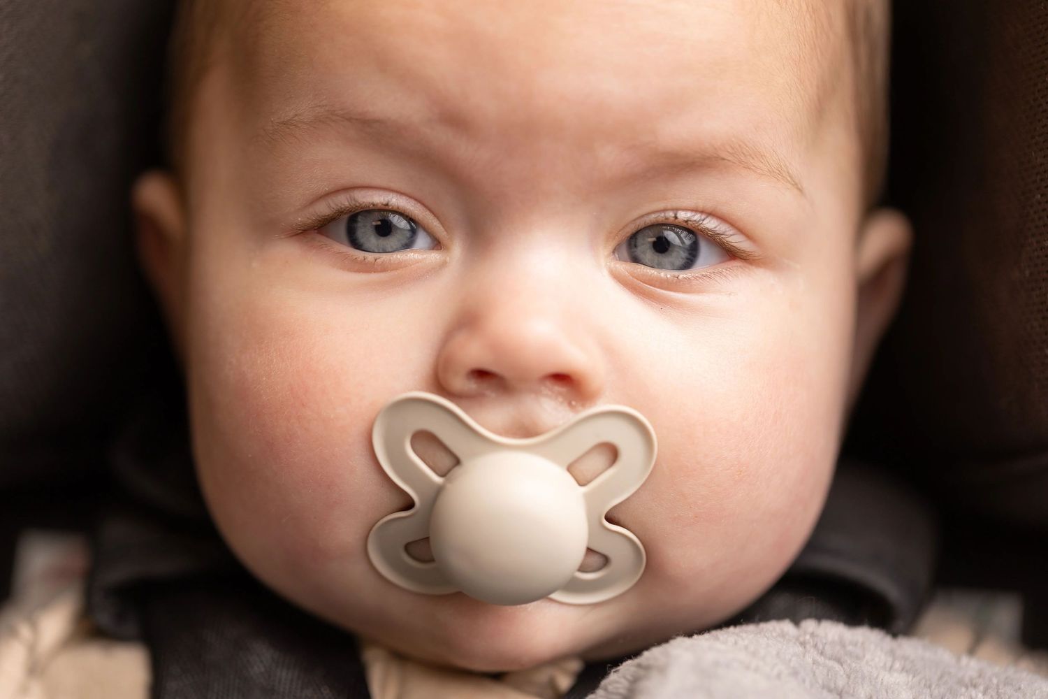Baby with pacifier photographed in soft lighting against dark background.