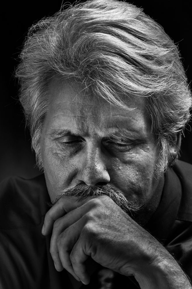 Dramatic black and white portrait of a contemplative expression with windswept grey hair.