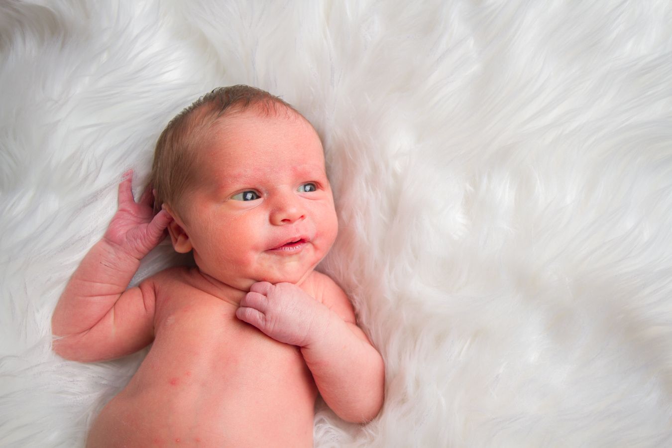 Newborn baby lying on soft white fur background during professional photo session.