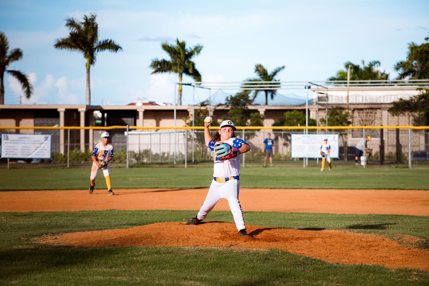 Baseball player in batting stance preparing to hit on baseball diamond with palm trees in background.