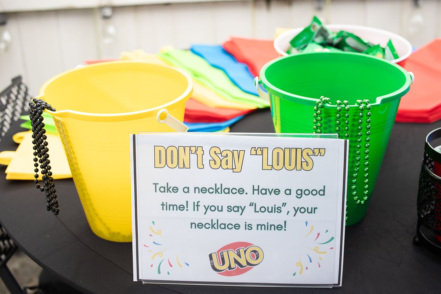 Party game sign with colorful plastic cups and necklaces for an UNO-themed celebration.