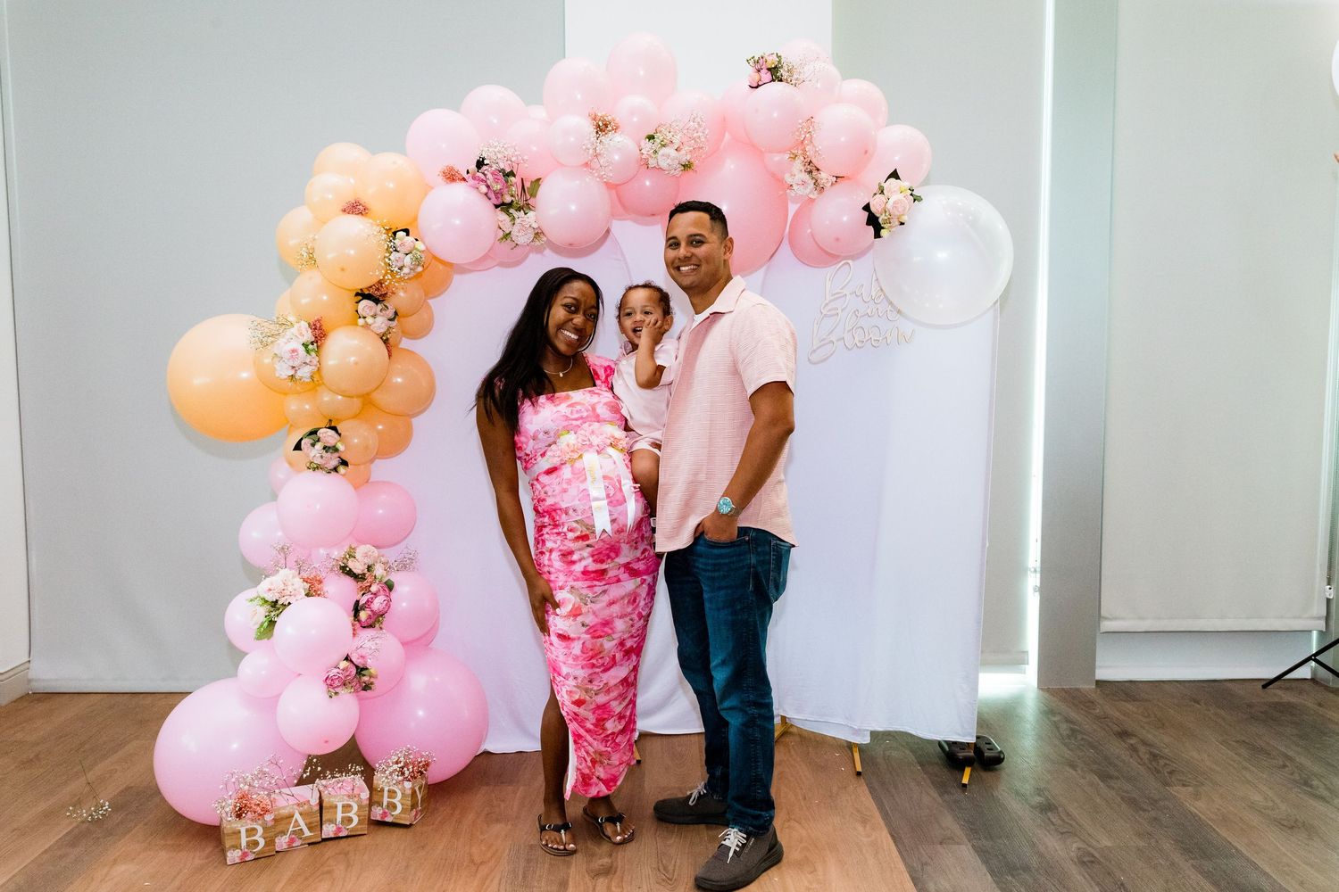 Pink and peach balloon decorations arranged along a white wall for an event.