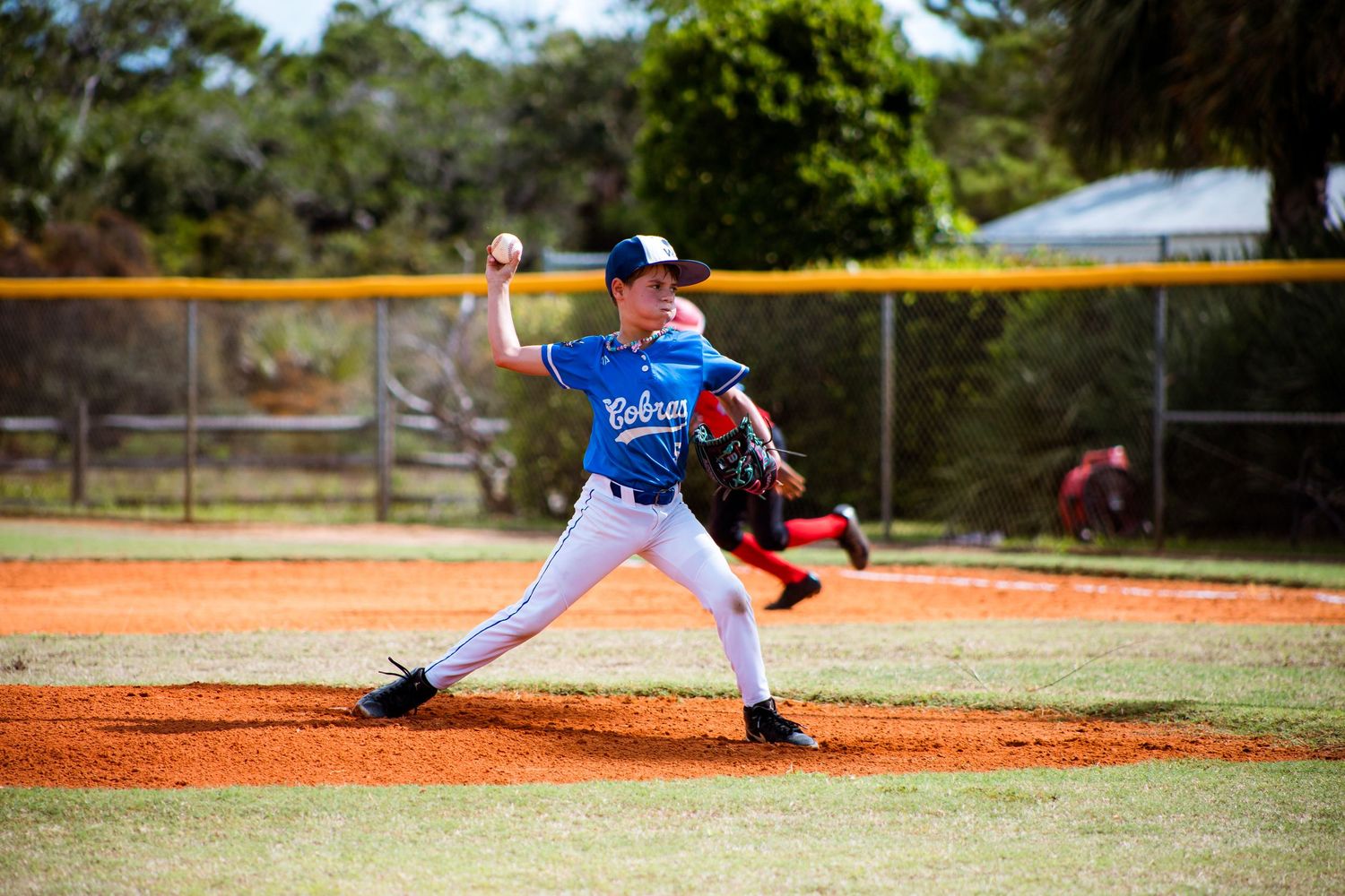 Youth baseball pitcher in blue jersey winds up to throw from the mound during a game.