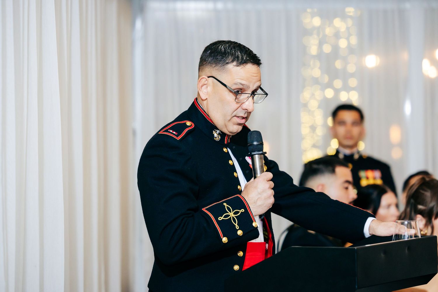 Marines in dress uniforms deliver speeches at a formal military celebration.