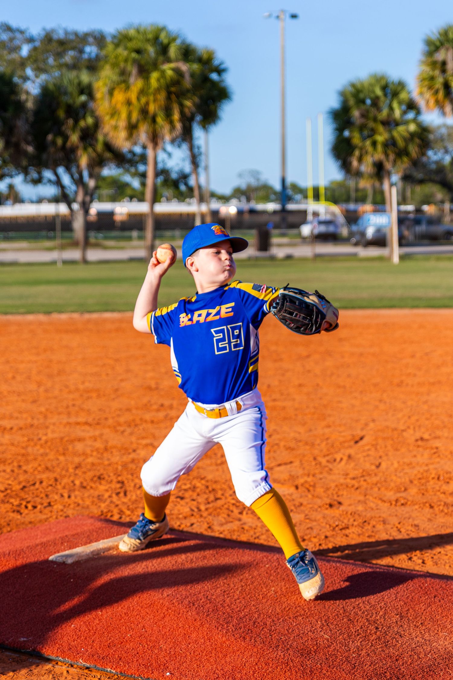 Baseball pitcher in blue uniform demonstrates pitching motion sequence on red clay mound during practice session.