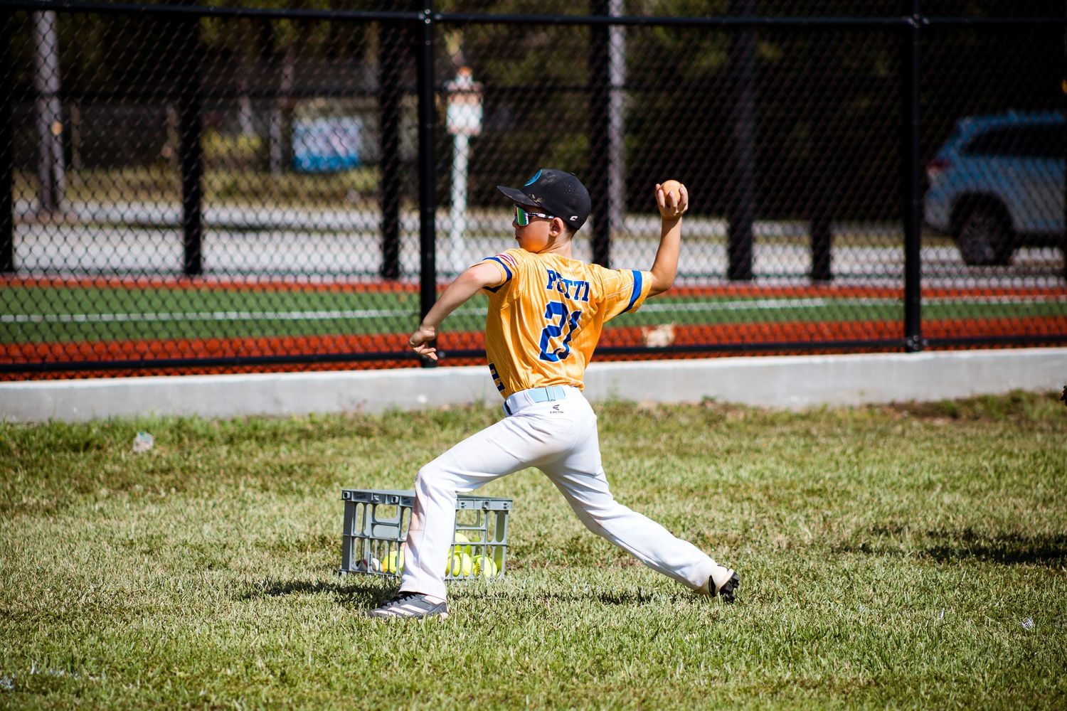 Baseball player in a yellow jersey practicing pitching form on a grass field.