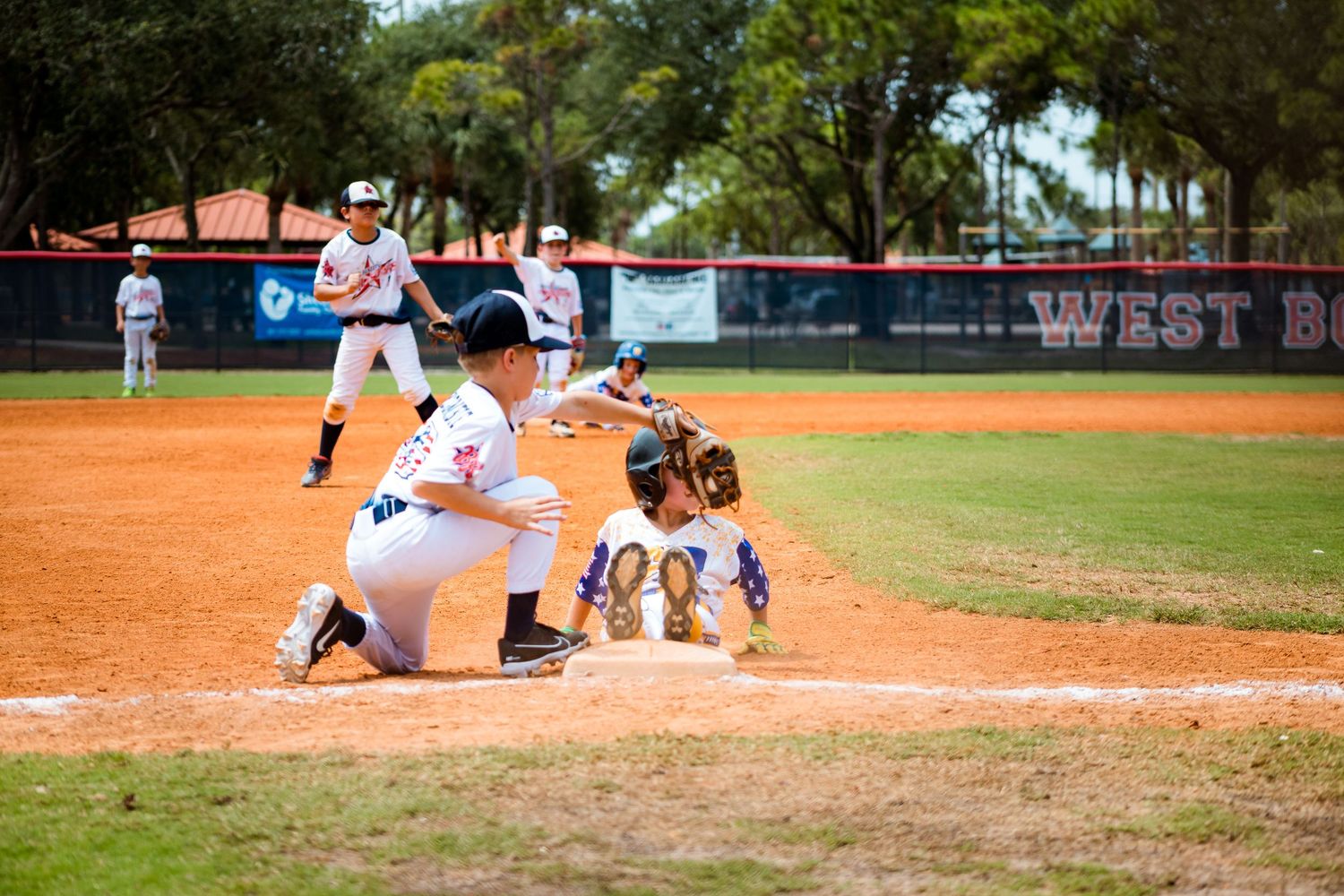 Baseball players in action at home plate with catcher crouching and batter preparing to swing on dirt field.