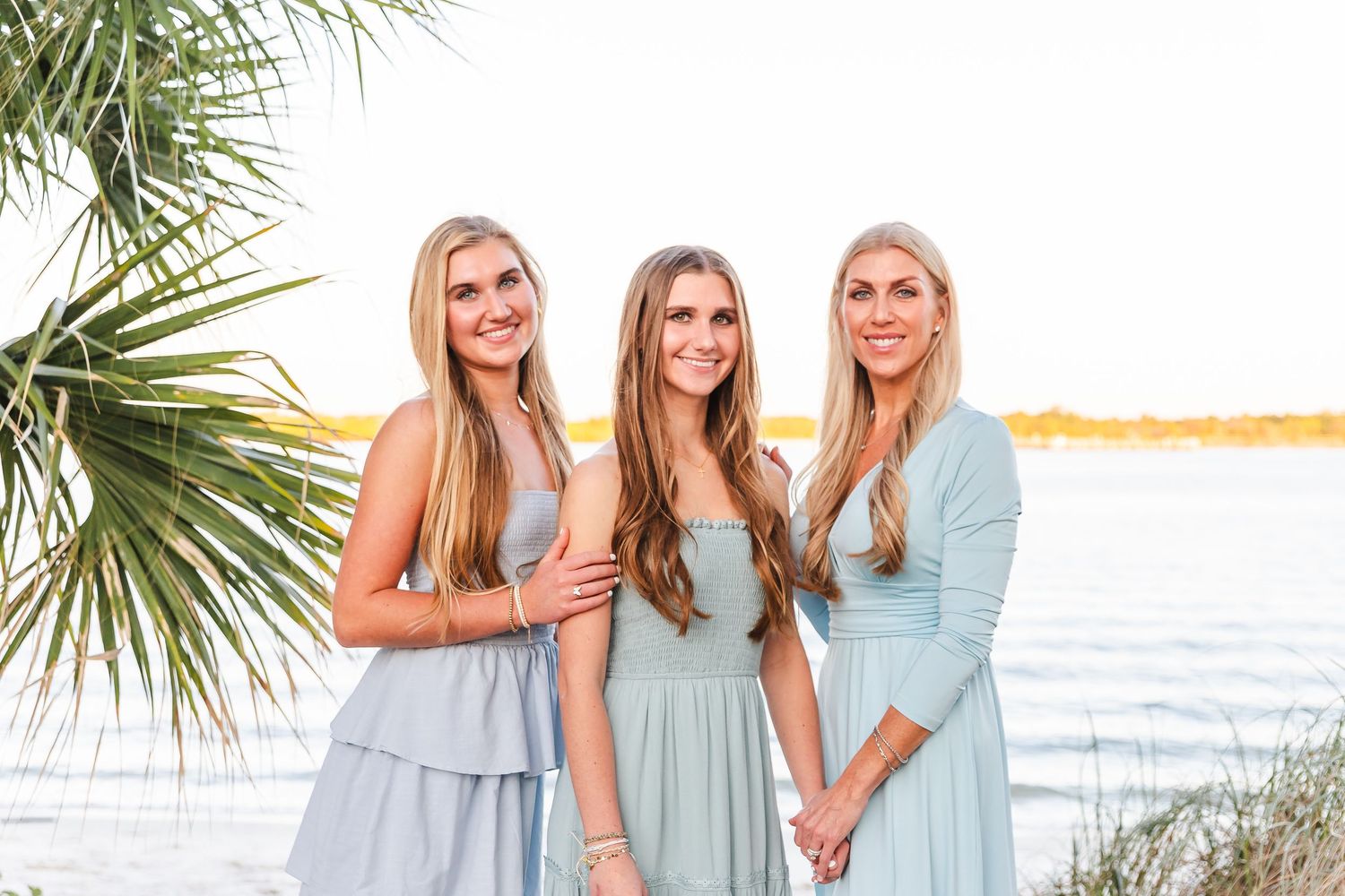 Family wearing coordinated blue and mint outfits poses together on beach at sunset.