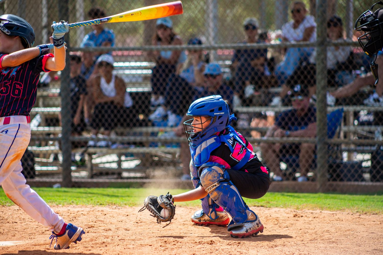 Youth baseball player swings a bat during a game while catcher and umpire watch from behind home plate.
