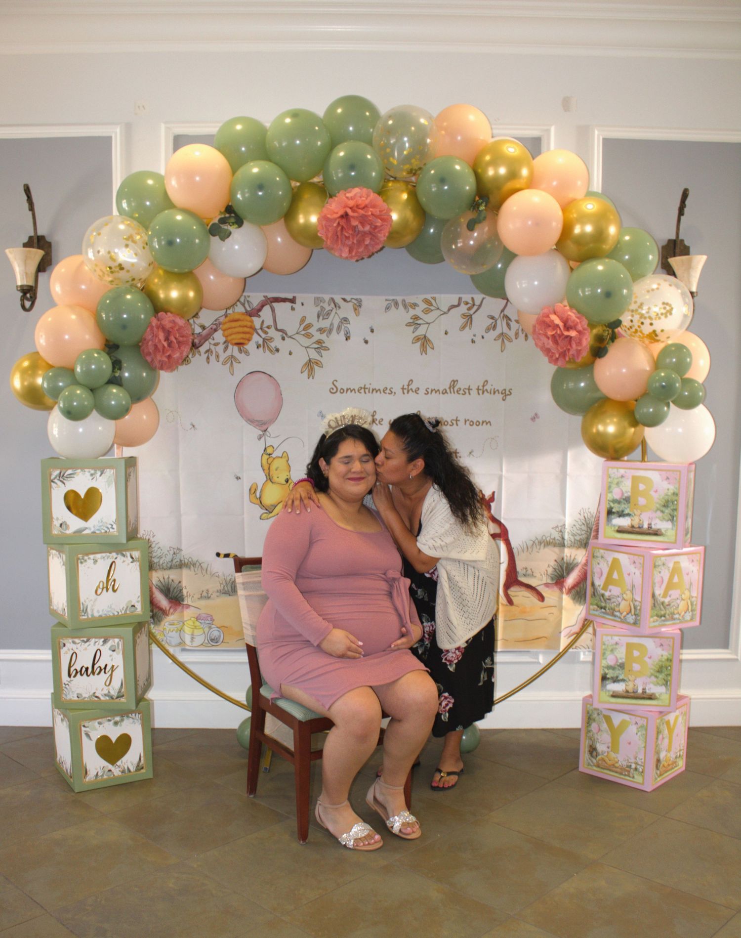 Baby shower celebration setup with balloon arch in sage green, peach and gold with decorative alphabet blocks.