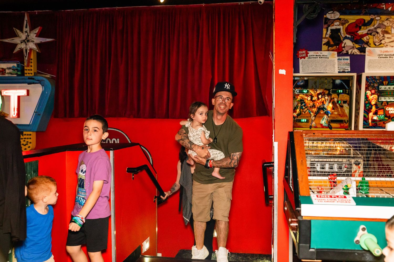 An image of a family standing on a stage with a red curtain backdrop and various toys and decor in the background.