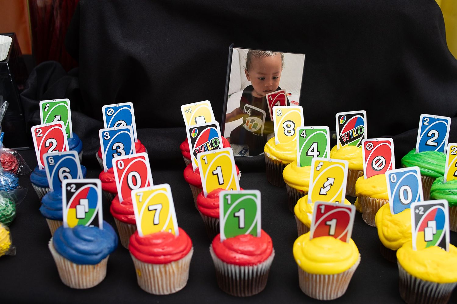 Colorful cupcakes decorated with UNO card game pieces arranged neatly on a black surface.