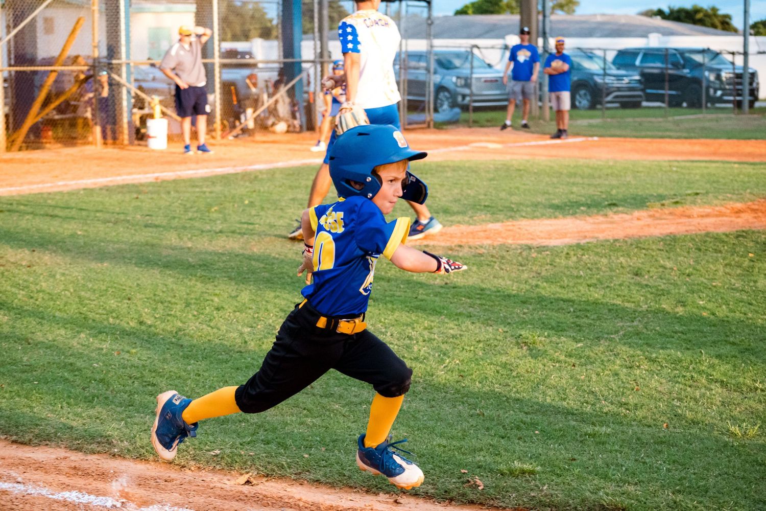 Youth baseball player in blue and yellow uniform running through batting motion during game.