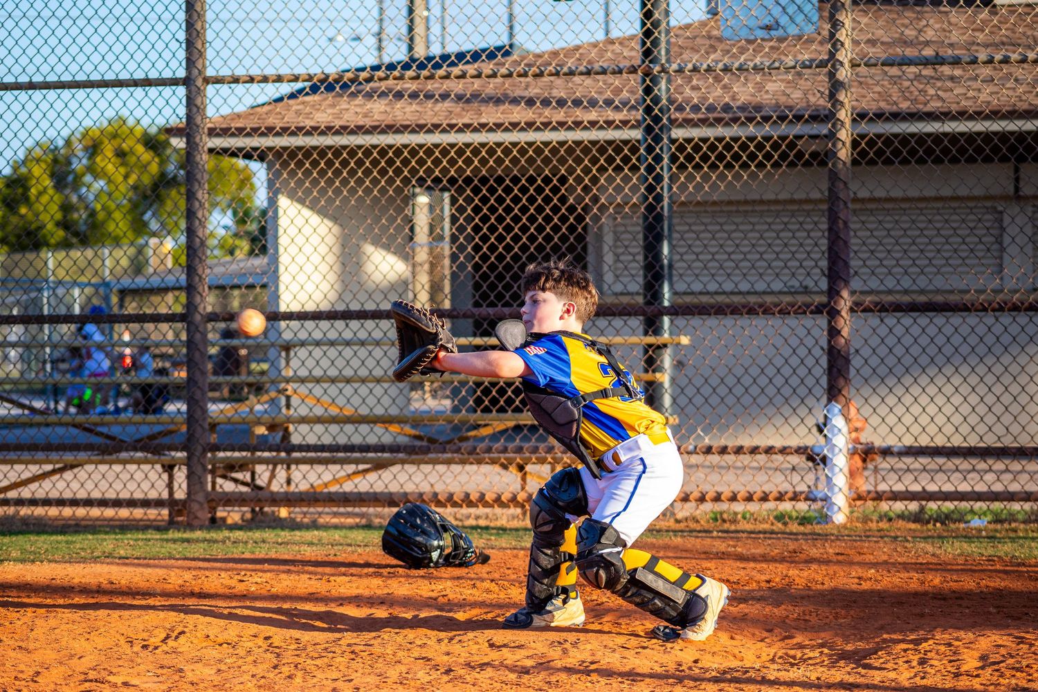 Baseball batter swings at pitch during game while catcher crouches behind home plate on dirt field.