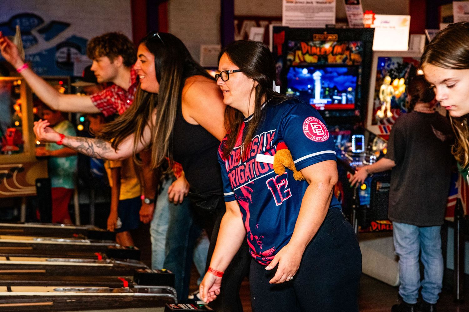 A group of people playing video games together in an arcade, with colorful neon lights in the background.