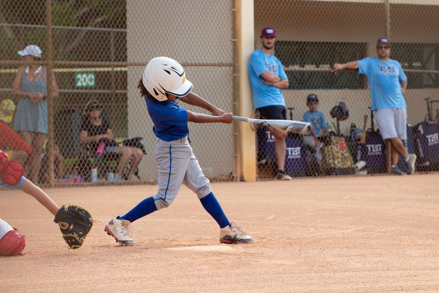 Youth baseball player in blue and white uniform swinging bat on dusty field.