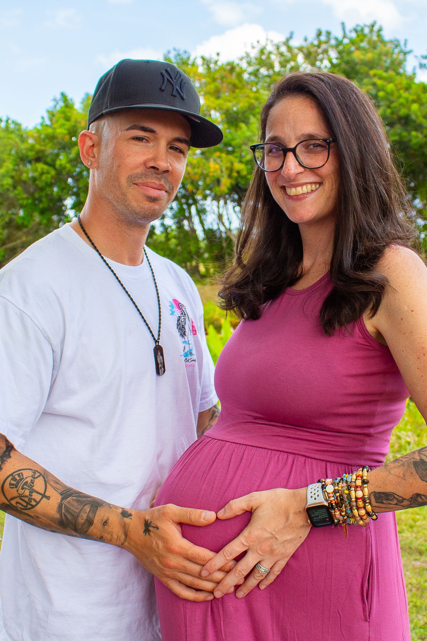 A couple sharing a tender pregnancy moment outdoors in casual attire.