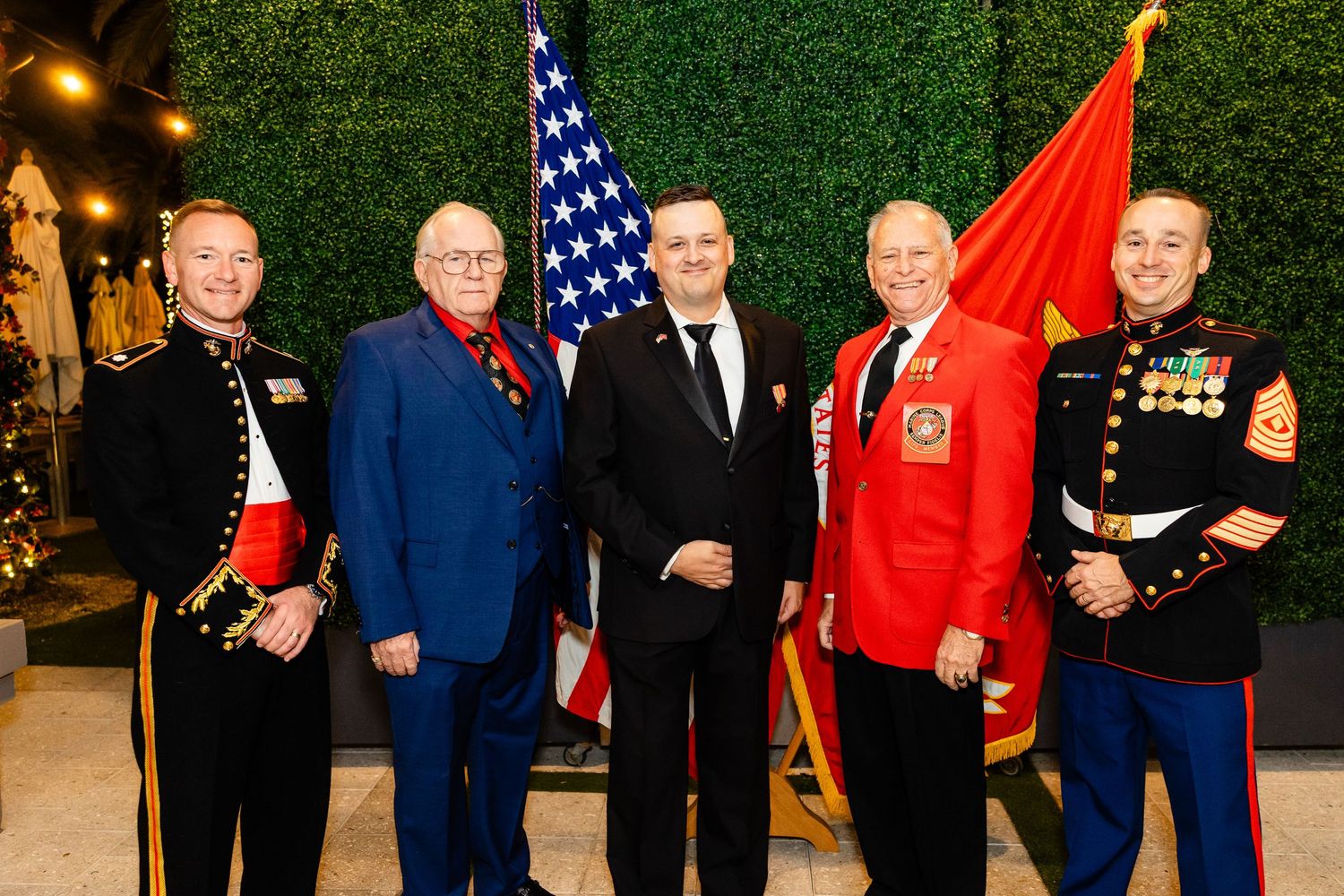 A group poses together at a formal event with American flags and a red banner in the background.
