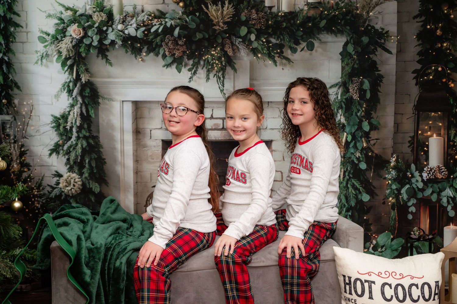 A group wearing matching holiday pajamas sits together on a white bench surrounded by winter greenery and decorations.