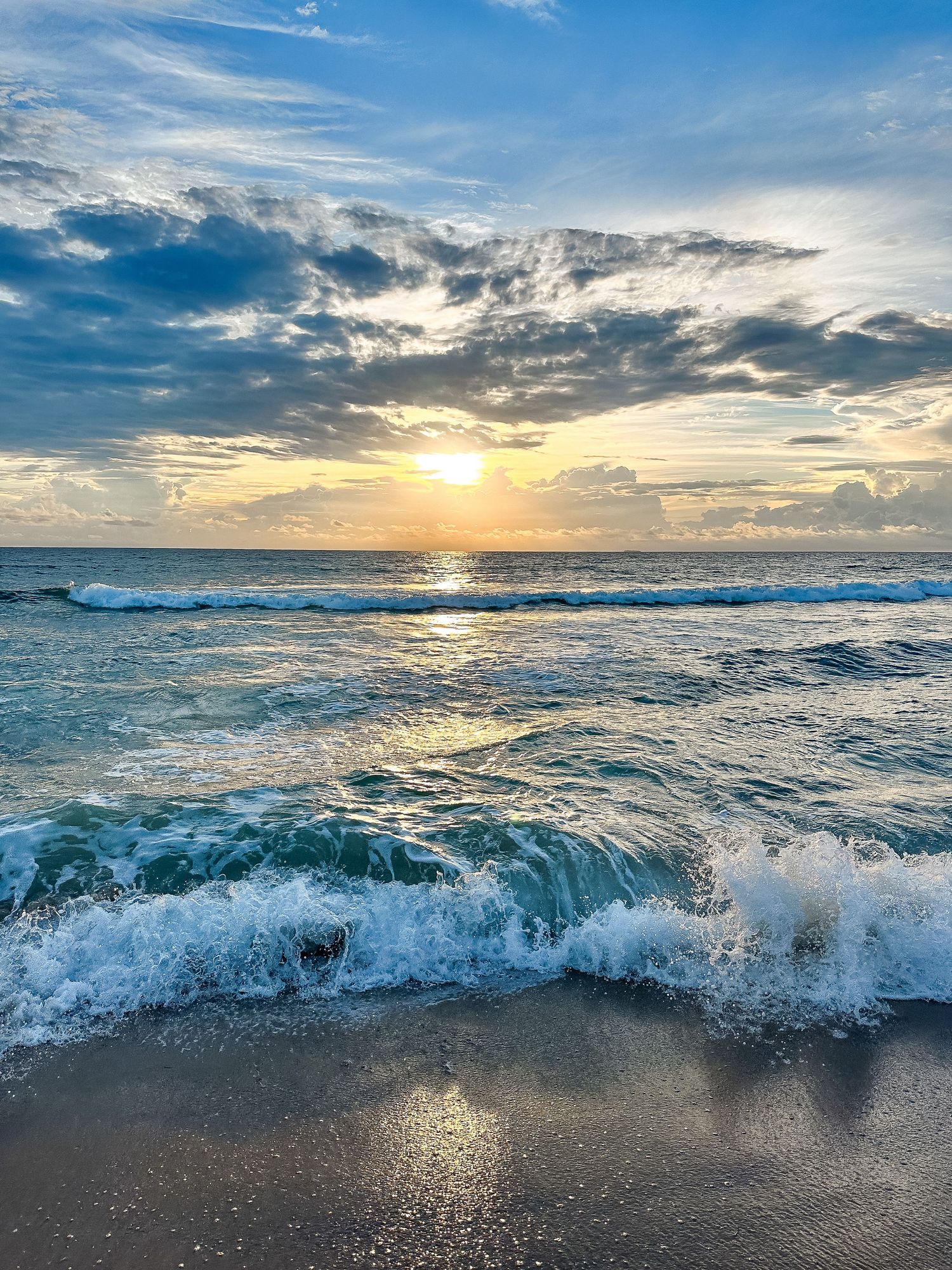 Golden sunlight breaks through clouds over rolling ocean waves at sunset.