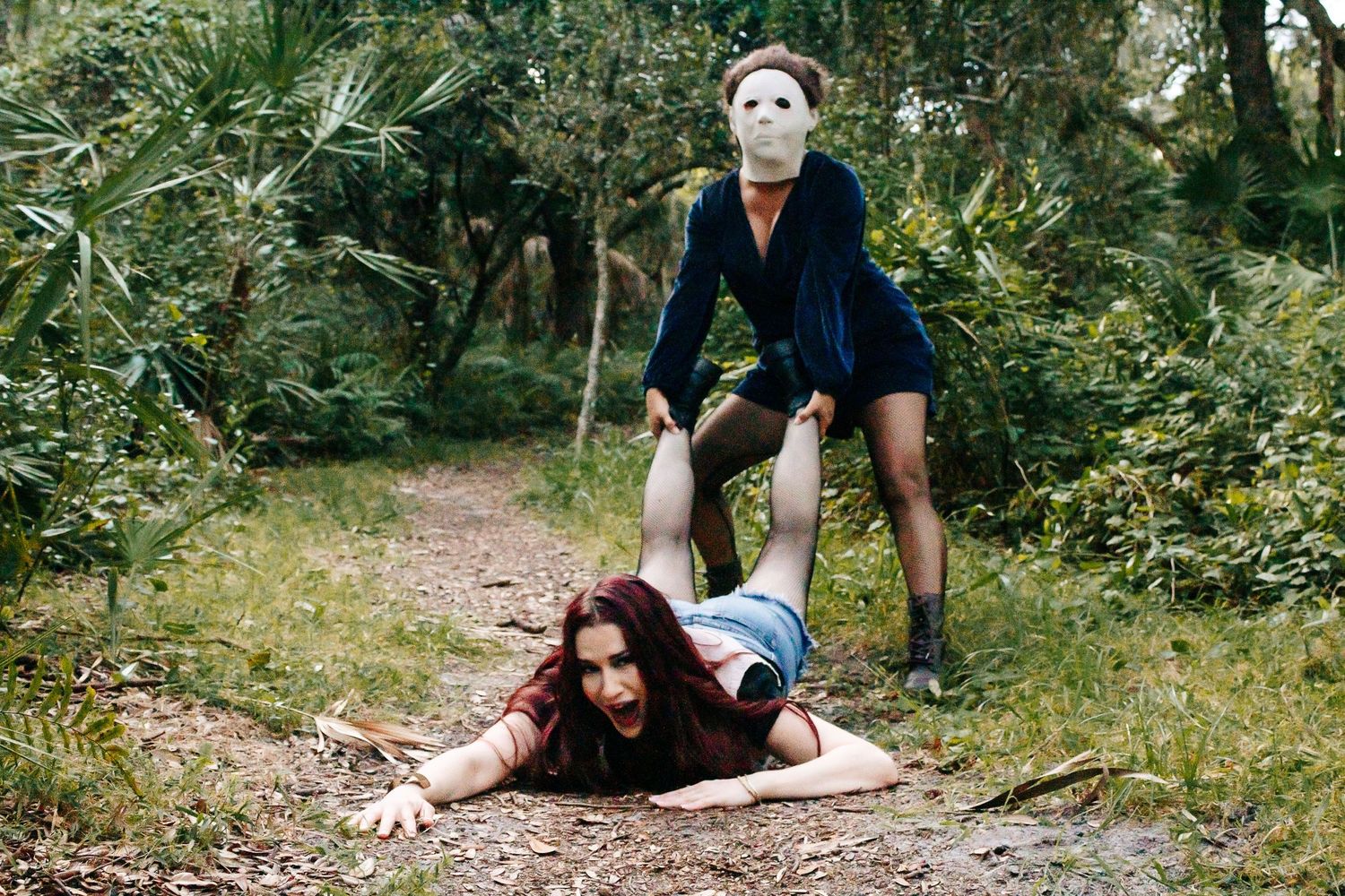 Two figures in masks enact a dramatic scene on a forest path.