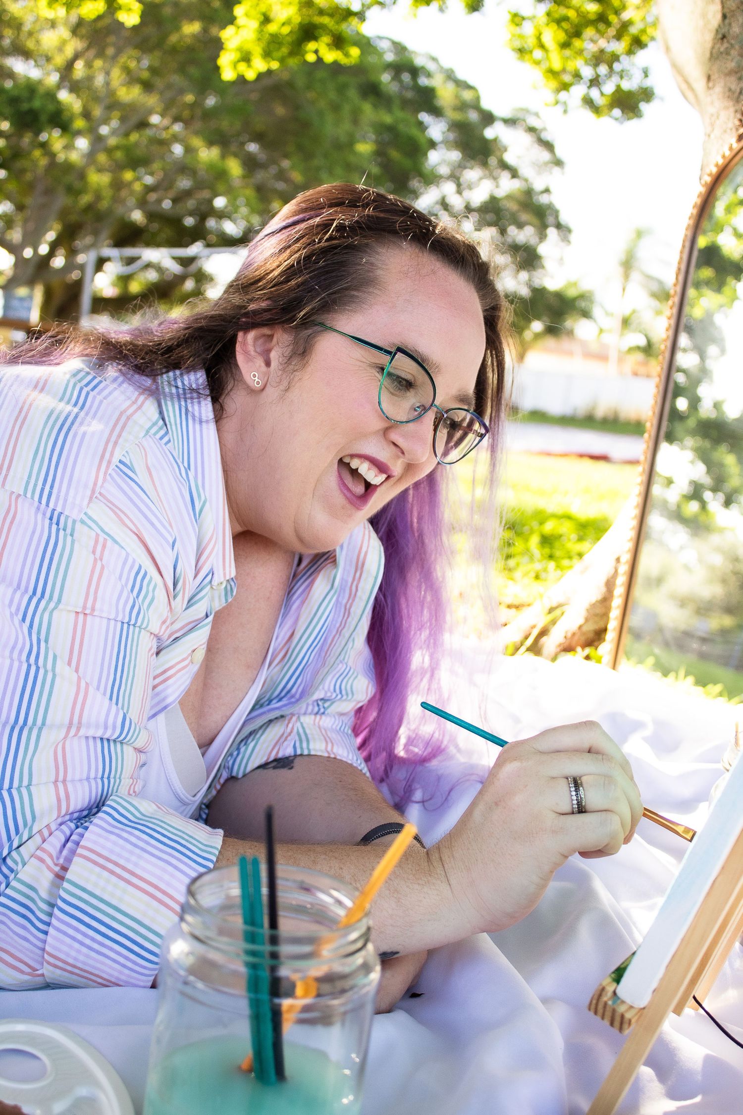 Artist working on a creative project outdoors with art supplies and a glass of water.
