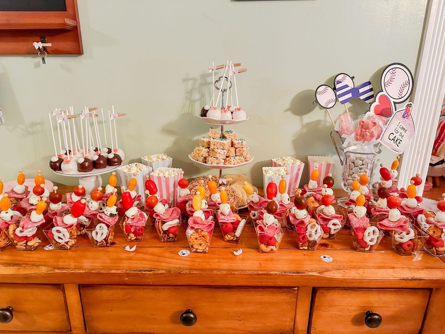 Pink and white themed party dessert table with cake pops and sweet treats on wooden furniture.