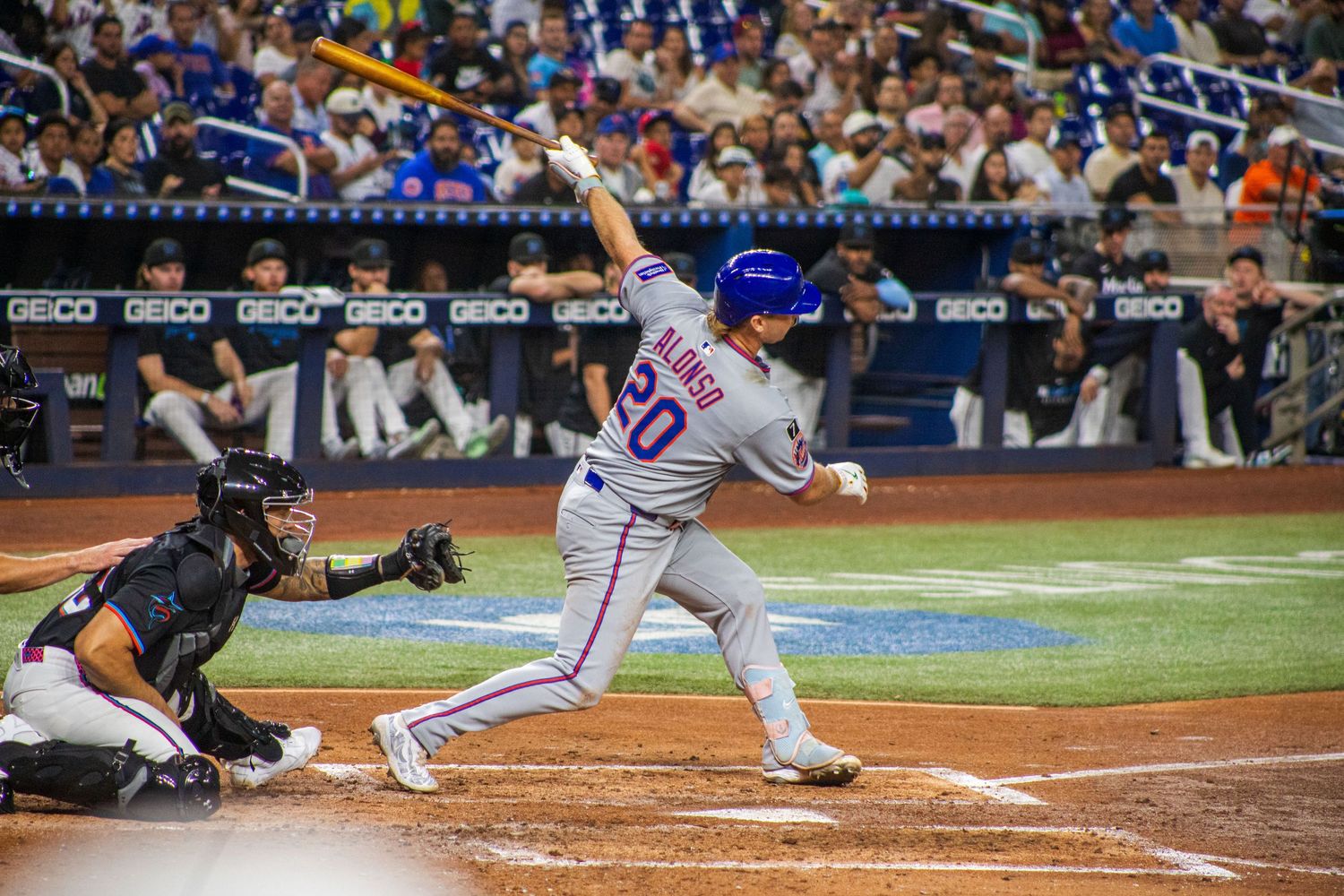 Baseball players compete at home plate during night game with stadium lights illuminating the field.