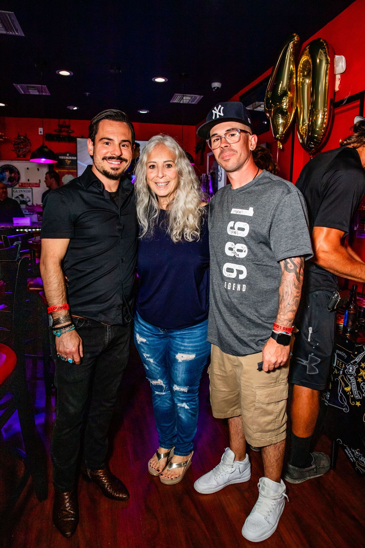 A group photo of three people, two men and one woman, posing together in a brightly lit and decorated entertainment venue.
