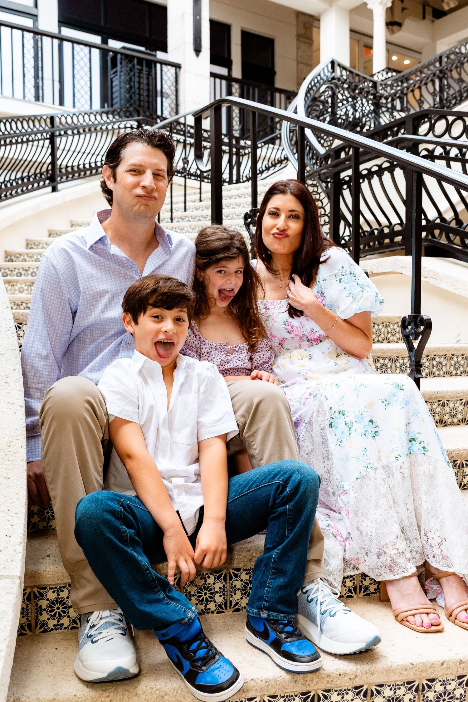 Family of four sitting on decorative tiled steps, smiling and making fun faces.