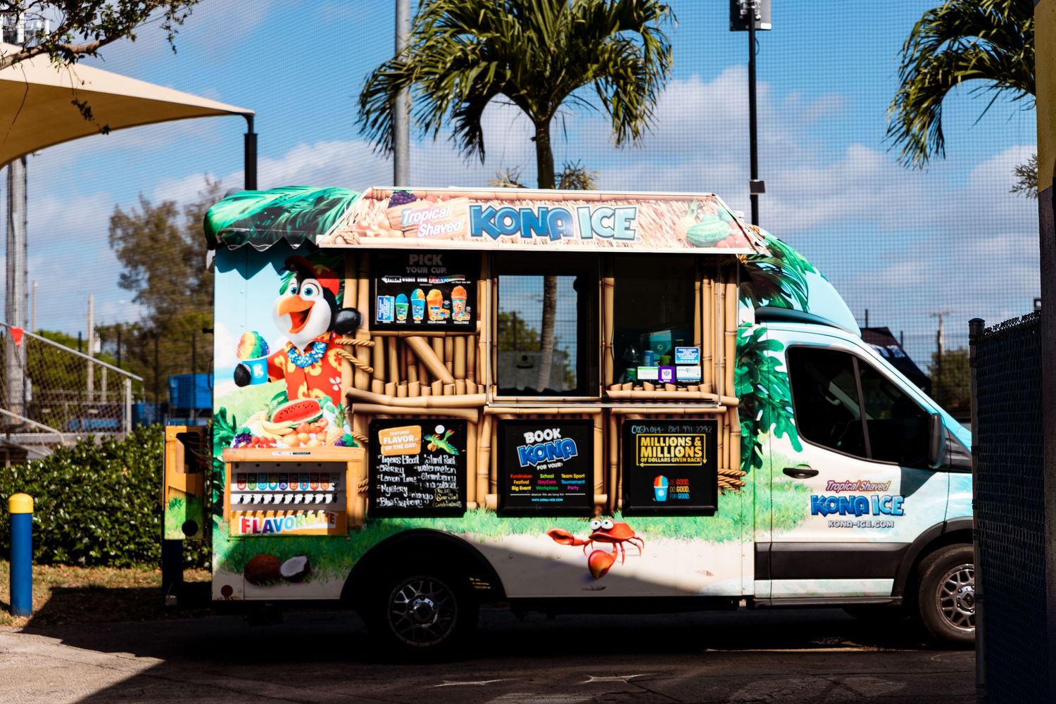 A white ice cream food truck decorated with colorful graphics and palm trees parked under a sunny sky.