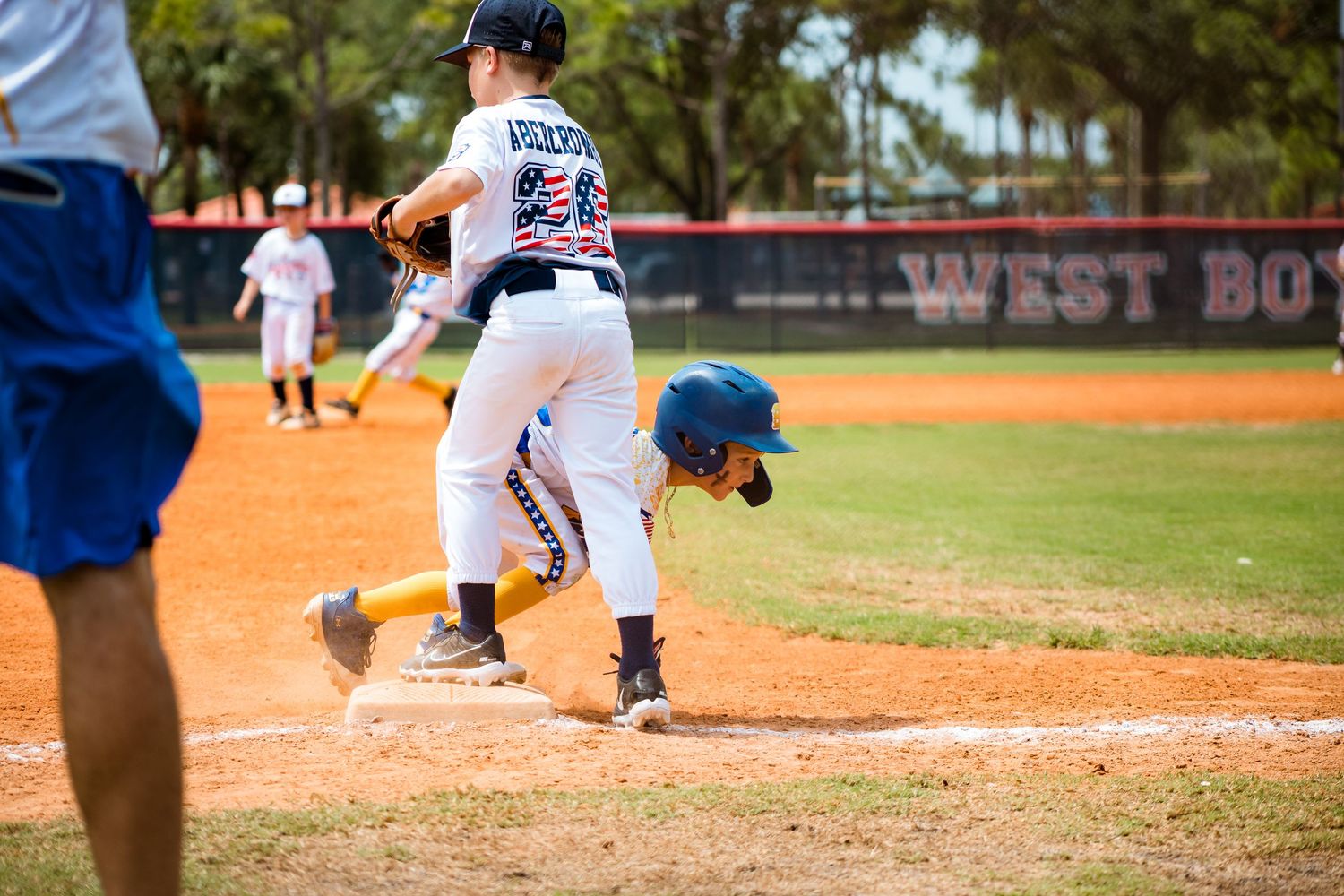 Baseball batter in striped uniform follows through on swing at home plate during daytime game on dirt field.