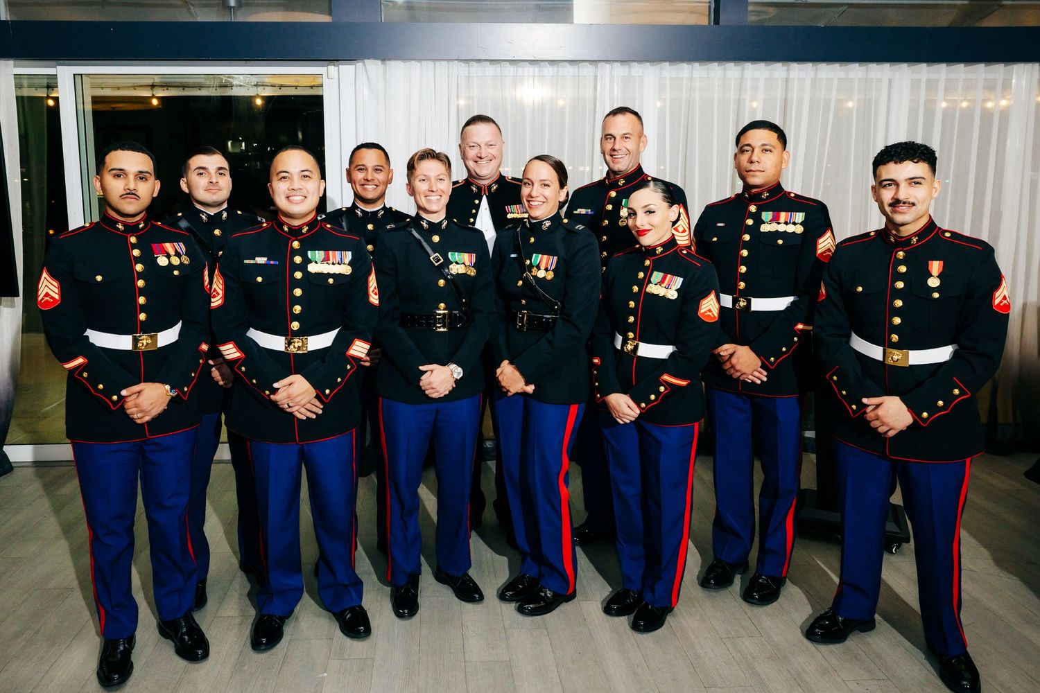 Large group of Marines in dress blues pose together in formation for a ceremonial photo.