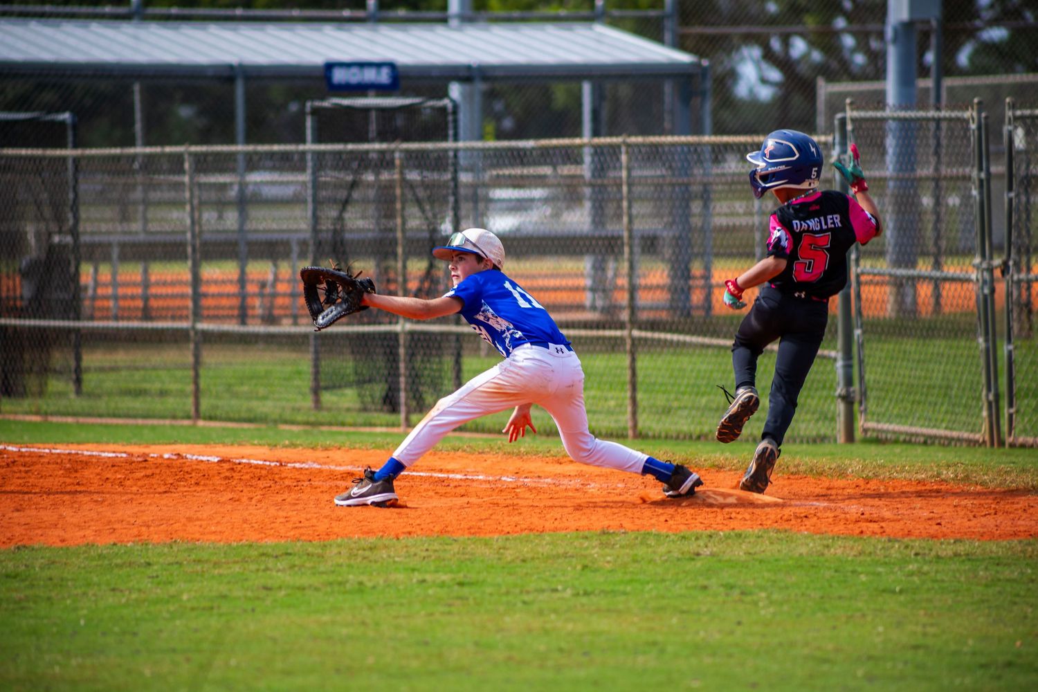 Baseball players in action during a game on a sunny day at a local baseball field with orange clay infield.