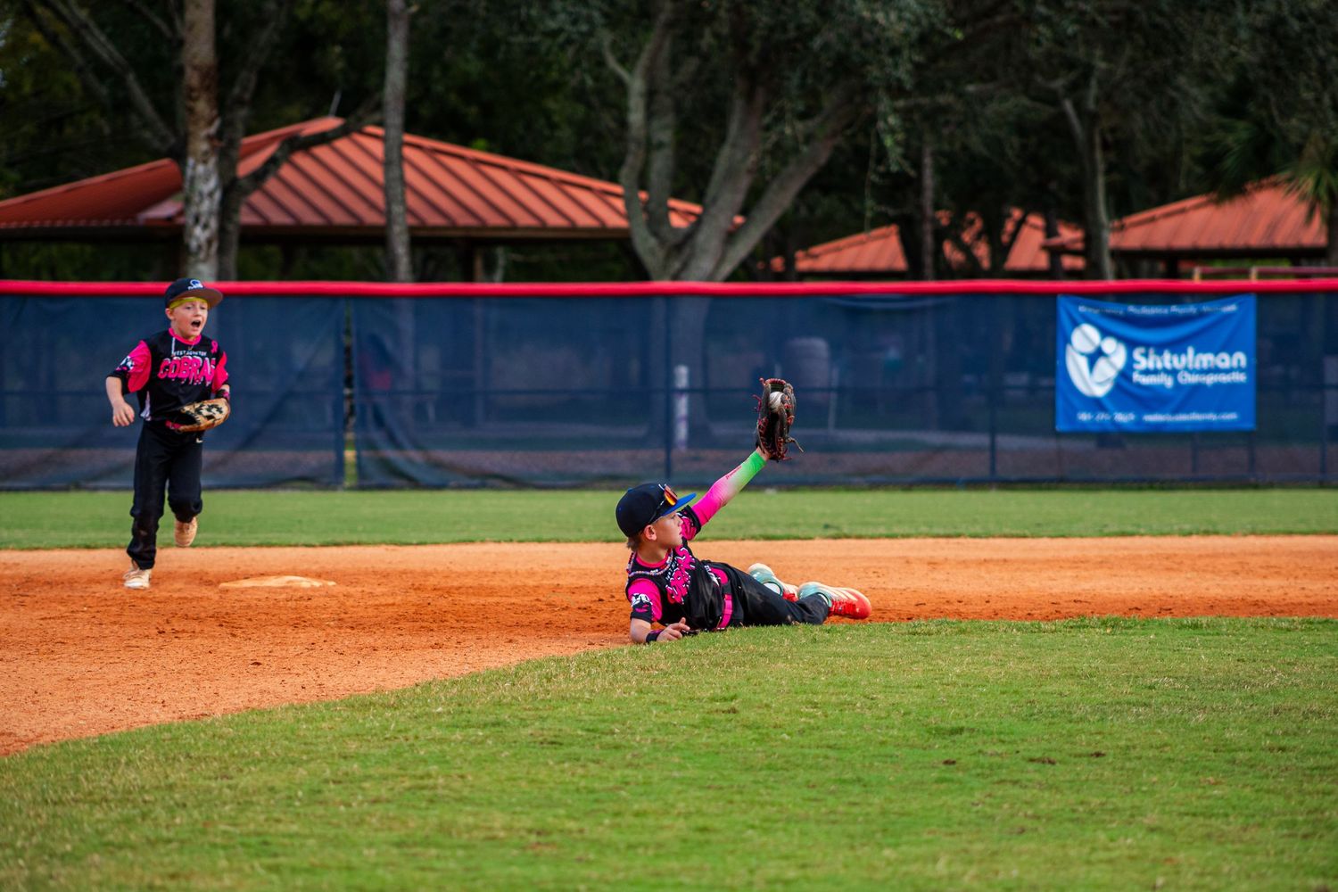 Baseball game in progress on a well-maintained field with orange clay infield and green outfield.