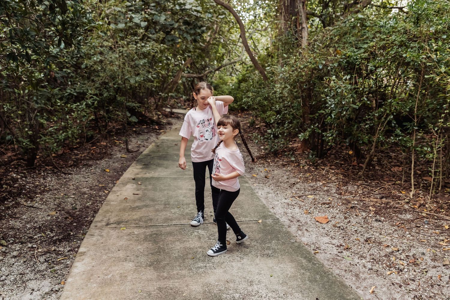 A group walks along a winding concrete path through a wooded area on a sunny day.