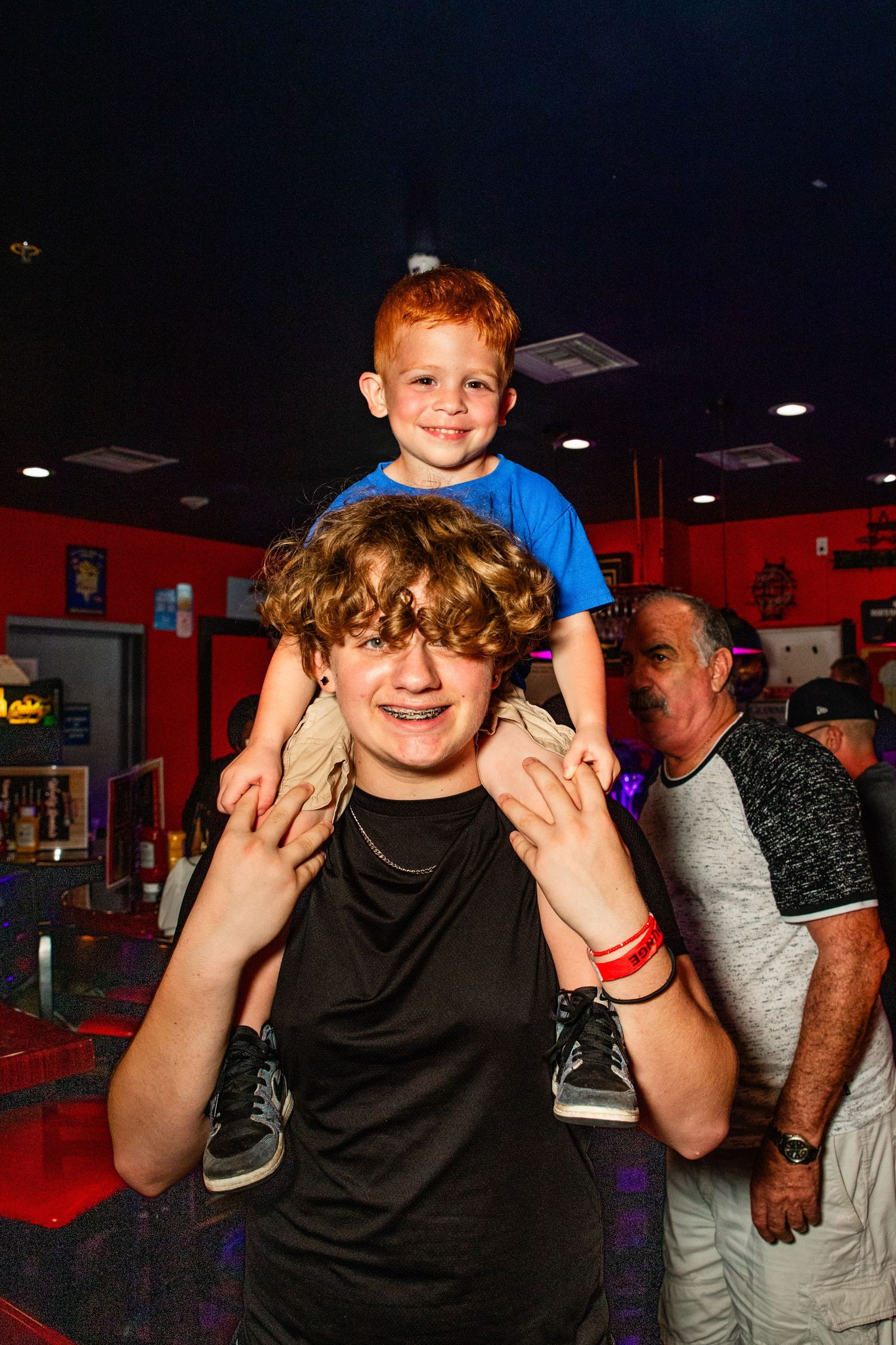 A young boy sitting on an adult's shoulders in a crowded and colorful entertainment venue.