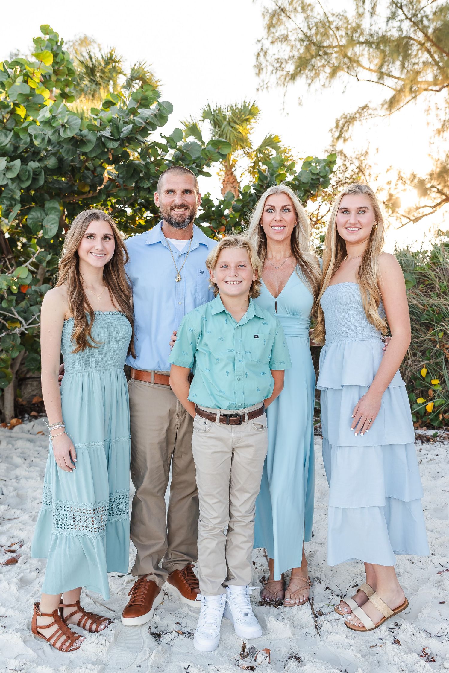 Family group wearing coordinated mint green and khaki outfits poses together on white sandy beach.