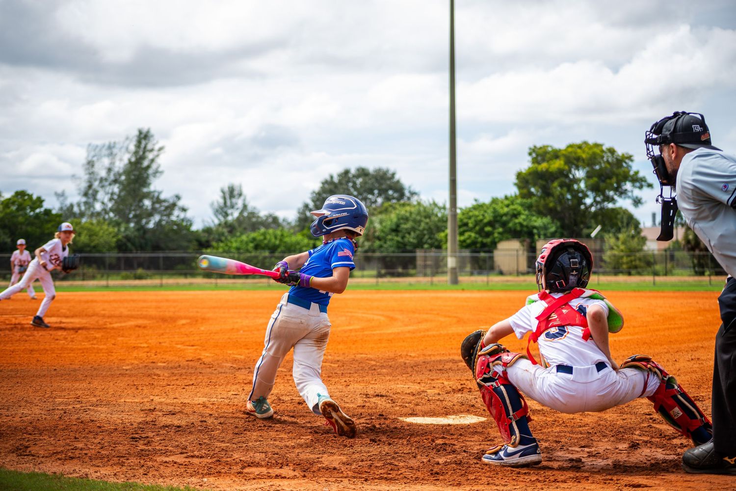 Baseball player sliding into base during intense game action on dusty orange infield dirt.