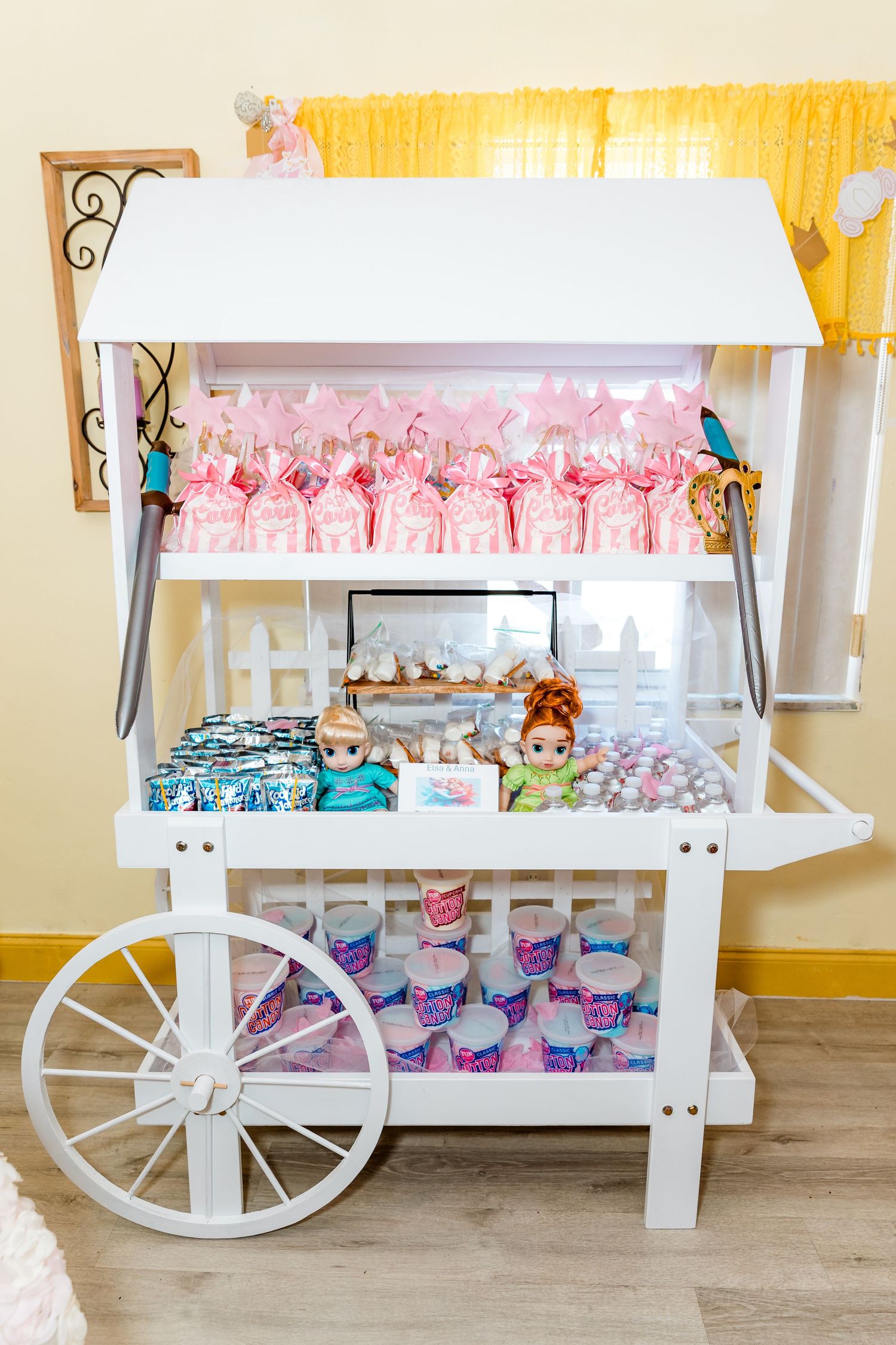 A decorative white cart display filled with pink party favor bags and treats at a themed celebration.
