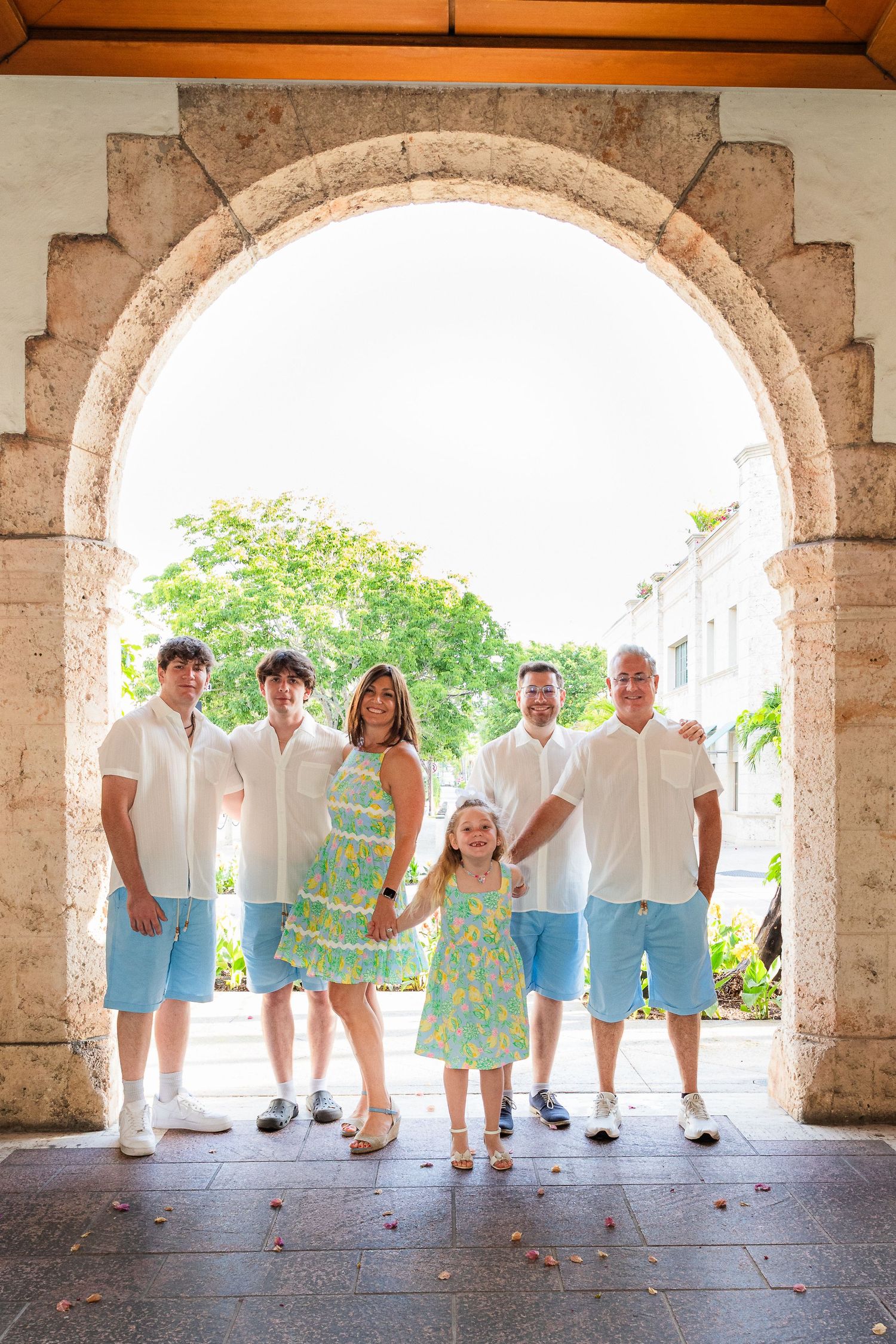 Group in coordinated white and blue summer outfits standing under a stone archway at a Mediterranean destination.