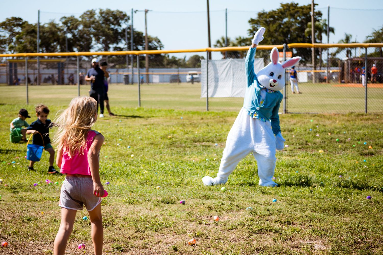 Children play outdoors with a costumed Easter Bunny character in a sunny field.