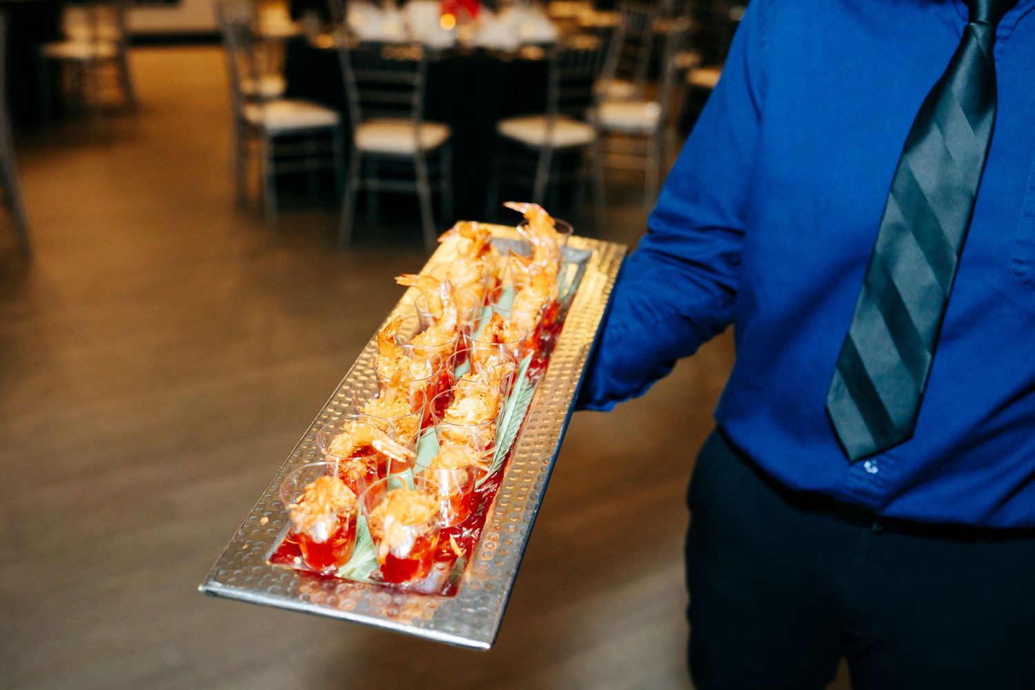 Server holding a tray of elegant lobster dishes on a silver platter in a dining room setting.