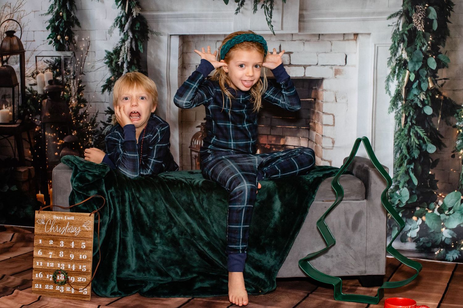 Two children in matching pajamas make silly poses on a green velvet couch.