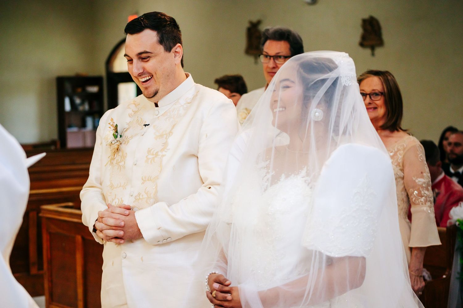 Couple stands at altar during Catholic wedding ceremony as bride wears traditional white veil.