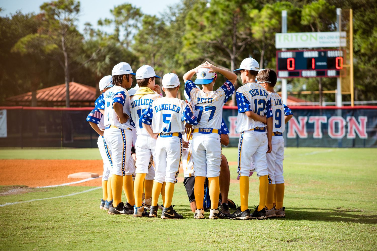 Baseball team members huddle together on sunny field during game day wearing blue and white uniforms.