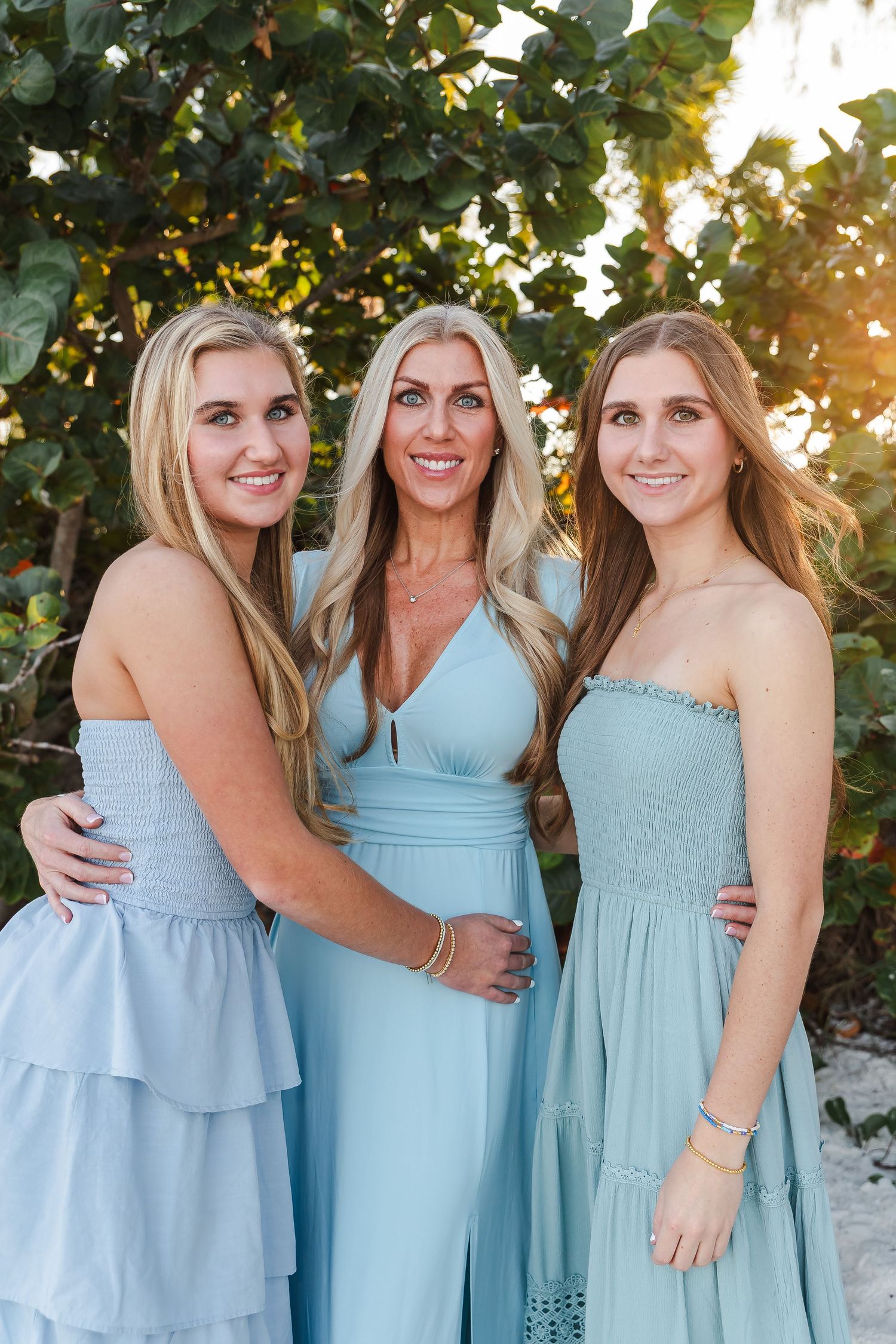 A group wearing coordinated light blue dresses poses together outdoors in warm sunlight.