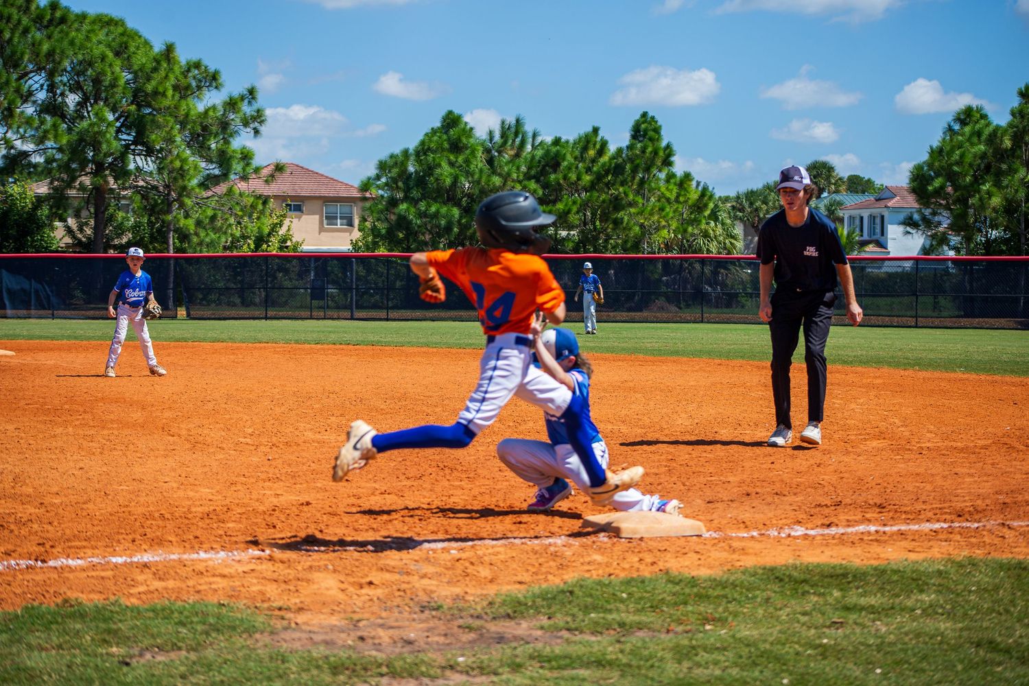 Baseball player in blue uniform slides into base as fielder attempts to make the tag during intense game play.