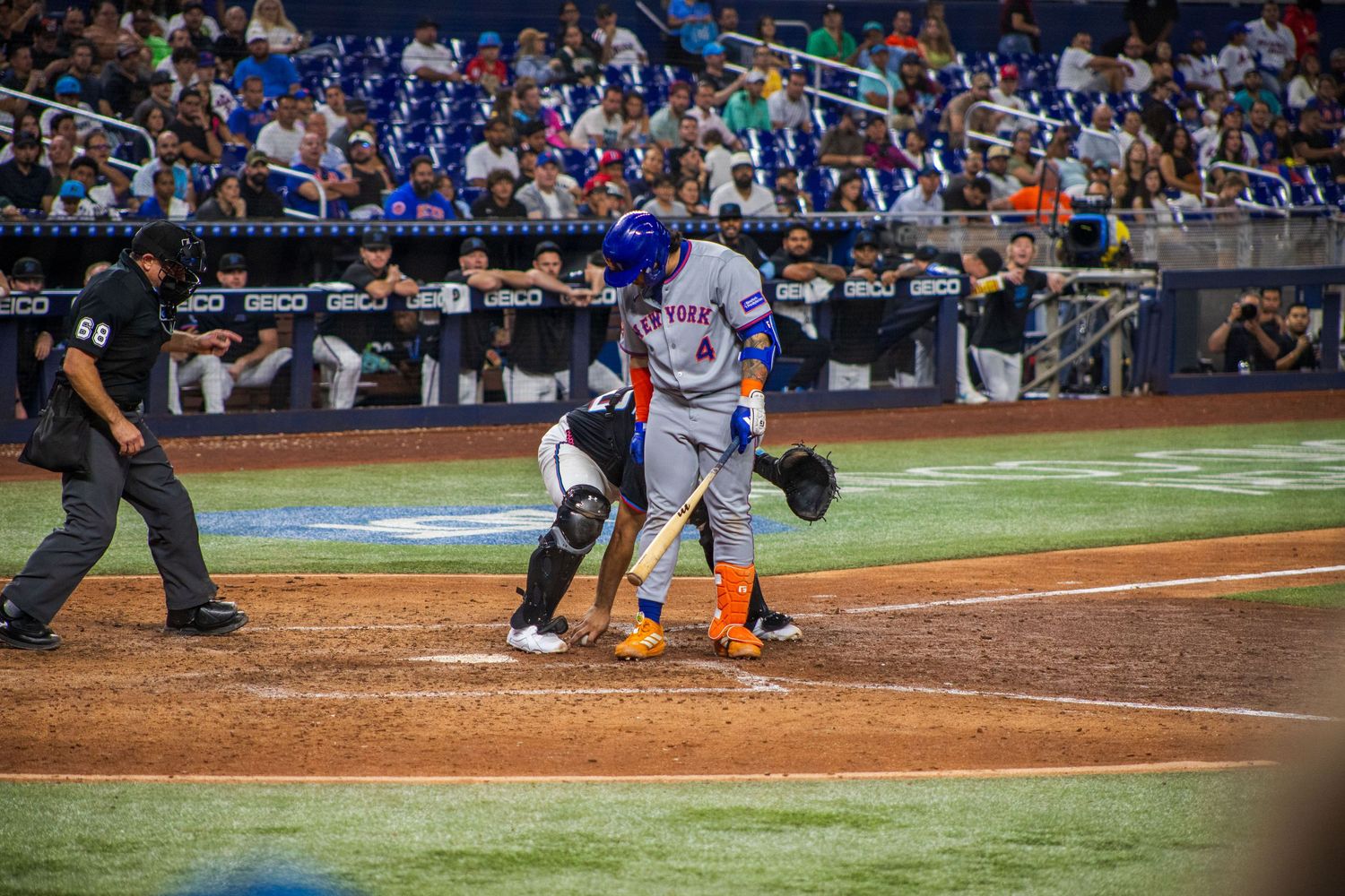 Baseball players positioned around home plate during competitive play at crowded stadium.