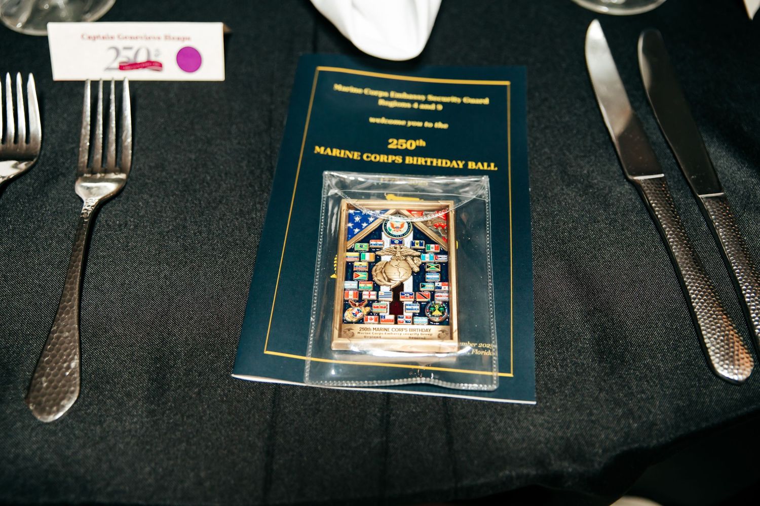 Place settings and programs arranged on dark tables at a formal military dining event.